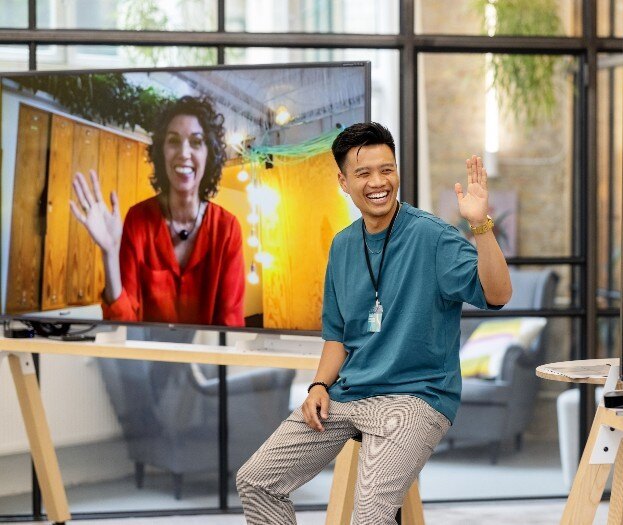 Young businessman waving to colleagues on screen